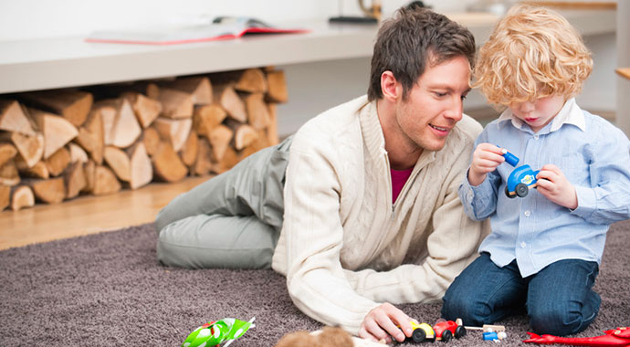 un homme allongé sur un tapis joue avec son enfant avec des voiturettes