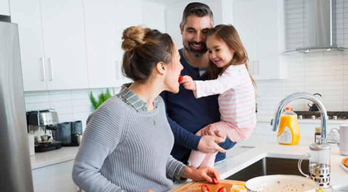 Une fille dans les bras de son père donne une fraise à sa mère qui prépare une salade de fraise