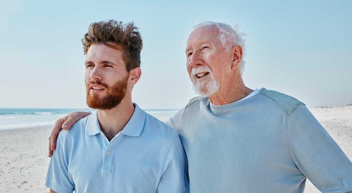 Une jeune homme et son grand père se promènent sur la plage.