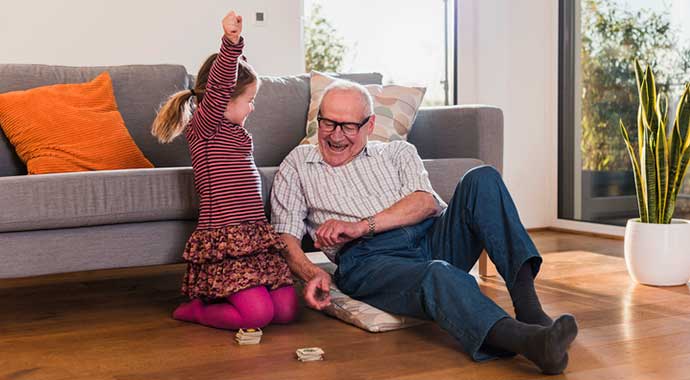 Un retraité et sa petite fille jouent ensemble à un jeu de société et la petit fille jubile en levant le bras