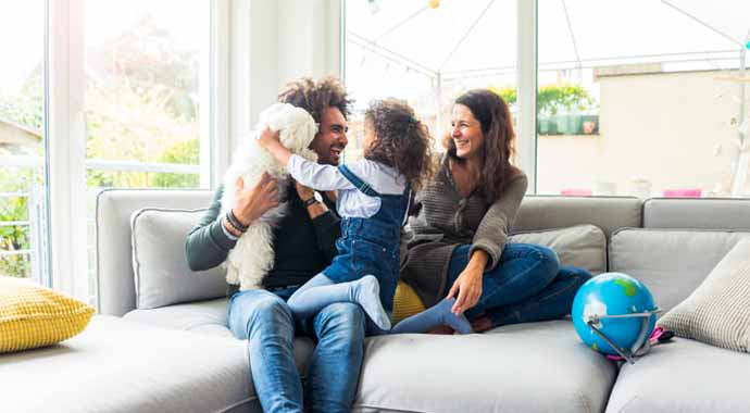 des parents et leur fille sur un canapé joue avec leur petit chien