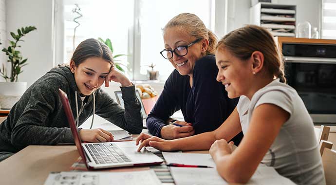 une femme aide des enfants à faire leurs devoirs dans la bonne humeur.