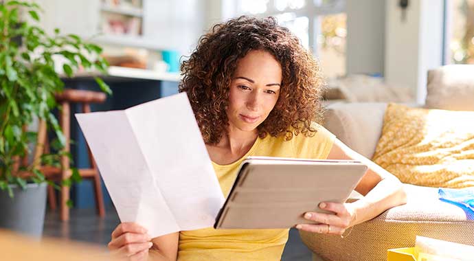 Une femme consulte sa feuille d'imposition et fait une comparaison avec sa tablette