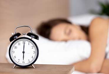 Focus sur un réveil avec une femme en sommeil en fond